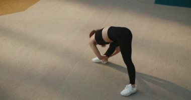 Egzersiz yapan, eğilip dışarı uzanan çekici genç bir kadın. Siyah spor giysili atletik kadın antrenman öncesi ısınıyor ya da ısınıyor. Sportif kız jimnastik yapıyor..