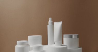 Stüdyoda kahverengi bir arka planda beyaz şişe ve kozmetik tüpleri. Doğal malzemelere dayalı kozmetik yağları, fırça, tonik, vücut bakımı. Saç ve cilt bakımı için doğal kozmetik üretimi.