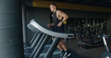 İyi donanımlı, çağdaş bir spor salonundaki koşu bandında koşan odaklanmış genç bir adam. Sağlık ve zindelik yaşam tarzı sergileniyor. Modern bir spor salonunda koşu bandında koşan genç adam.