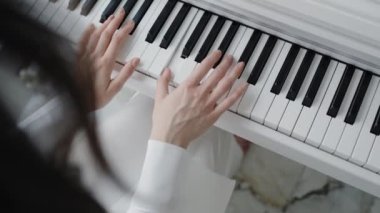 Beyaz piyano tuşlarında çalan ellerin yakın çekim görüntüsü huzurlu ve uyumlu bir atmosfer yaratıyor. Müzik, yaratıcılık ve rahatlama temaları için mükemmel. Eller Zarif Ayarlarda Piyano Çalıyor