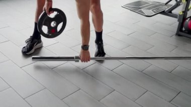 Spor giyimli bir sporcu halteri kavrıyor, kaldırmaya hazır, bir spor salonunda güç ve kararlılık gösteriyor. Spor salonunda Halter Hazırlamaya Odaklanmış Sporcu