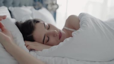 Huzurlu kadın sabah ışığıyla yatakta dinleniyor. Huzur ve rahatlama göstergesi. Huzurlu Kadın Konforlu Yatak Odasında Beyaz Çarşaflarla Yatakta Rahat Uyuyor