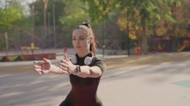 Spor kıyafetlerine odaklanmış genç bir kadın kollarını uzatarak sonbahar yapraklarıyla süslenmiş güneşli bir parkta antrenmana hazırlanıyor. Park 'ta Açık Hava Esneme Egzersizleri Yapan Genç Kadın