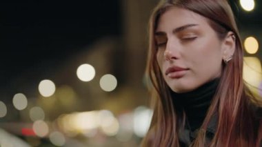 Gece lambalarının arka planında genç bir kadının portresi. Şehir, gece, kız, ışık, dışarıda, akşam, yaşam tarzı, ayakta. Sokaktaki doğal güzellik kraliçesi. Yavaş çekim.