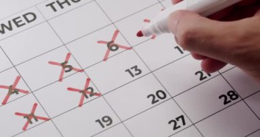 İlerlemeyi, takvimi, zaman yönetimini ve geri sayımı temsil eden kırmızı işaretli takvimde günleri işaretleyen bir elin yakın plan görüntüsü. Takvimdeki Günlerin Kırmızı İşaretle Üstünden Elle Silinmesi