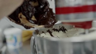 Bir fırıncının mutfak mikserine kalın, koyu çikolata hamuru dökerek pasta hazırlama sürecini ön plana çıkardığı yakın çekim. Zengin Çikolata Vurucusunu Pasta Hazırlama Karıştırıcısı 'na döküyorum.