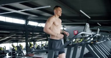 Geniş, iyi donanımlı bir spor salonunda koşu bandında koşan odaklanmış genç erkek sporcu, adanmışlık ve fitness hedeflerini vurguluyor. Modern Spor Salonu 'nda Koşan Fit Genç Adam