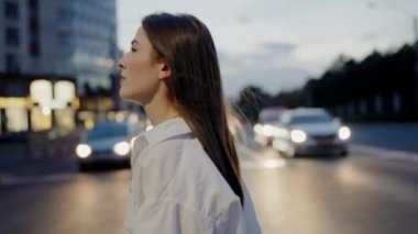 Beyaz bluzlu şık bir genç kadın alacakaranlıkta hareketli bir şehirde duruyor. Yüzü, arkasındaki trafiğin bulanık ışıklarıyla hafifçe aydınlatılıyor. Akşam Şehir Sahnesinde Zarif Kadın
