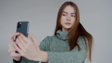 Kahverengi saçlı, yeşil balıkçı yaka giyen akıllı telefonuna odaklanmış genç bir kadının portresi. Balıkçı yakalı Genç Kadın Akıllı Telefon Kullanıyor