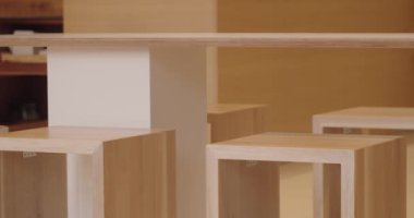 Minimalist ahşap tabure ve masaların yer aldığı çağdaş bir kafe. Temiz tasarımlar modern estetiği ve işlevselliği ticari bir ortamda vurguluyor, doğal ahşap dokusunu sergiliyor.