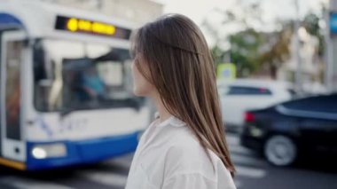 Genç, şık bir kadın şehir otobüsünün önünde kendine güvenle duruyor, şehir hayatını ve toplu taşımayı simgeliyor. Beyaz Gömlekli Genç Kadın Otobüsün Önünde Poz Veriyor