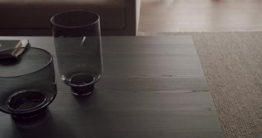 Siyah ahşap bir masanın üzerinde minimalist ve modern tasarımı vurgulayan iki siyah bardağın yer aldığı stilistik bir görüntü. Çağdaş Koyu Cam Kupalar Siyah Ahşap Masada