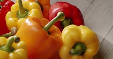 Kırmızı, sarı ve turuncu çeşitleri de içeren taze, renkli dolmalık biberlerin yakın plan çekimi, ahşap bir yüzeye yayılmış, güneş ışığı altında yakalanmıştır. Tahta Arkaplanda Taze Renkli Çan Biberleri