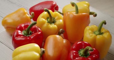 Açık ahşap bir yüzeyde kırmızı, sarı ve turuncu dolma biberlerin renkli çeşitleri sergilenmektedir. Yemek pişirmek, sağlıklı beslenmek ve yemekle ilgili konular için ideal. Canlı Bell Biberleri Çeşmesi