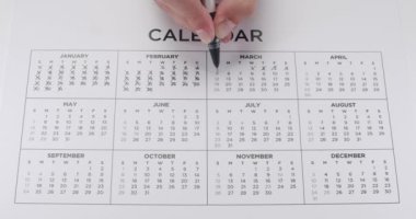 12 aylık takvimde el işaretleme günlerinin yakın plan, takip zamanı ve zaman çizelgesini sembolize ediyor. Kalem, Takip Süreci ve Planlarıyla Bir Takvim Üzerinde Günleri İşaretleyen Kişi