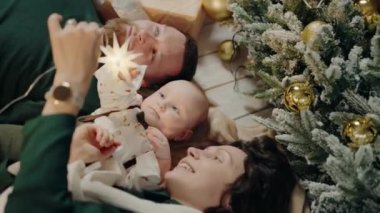Noel ağacının yanında yerde yatan ve tatilin tadını çıkaran mutlu bir aile. Fotoğraf sıcaklığı, aşkı ve Noel 'in neşesini yakalıyor. Mutlu Aile Yeni Yıl Kutlaması