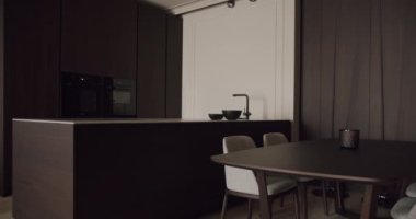 Koyu ahşap dolaplı zarif modern mutfak, minimalist yemek alanı ve şık aletlerle yaşamak ve yemek yemek için sofistike ve şık bir yer sunuyor. Modern Karanlık Mutfak İçi