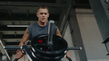 Kararlı kaslı bir adam modern bir spor salonunda ağırlık antrenmanı ekipmanlarıyla çalışıyor. Atmosfer adanmışlığı, gücü ve uygunluğu yansıtıyor. Kas Adam Spor Salonunda Yoğun Ağırlık Eğitimine Başladı