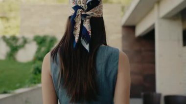 Kafasında desenli bir bandana olan genç bir kadın sıcak bir günde omzunun üstünden bakıyor. Sıradan ve düşünceli bir ruh hali. Bandana takan genç bir kadın omzuna bakıyor, sıcak bir gün.