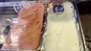 Gelateria 'daki bir konteynırdan dondurma topluyorum. Vanilya ve çilek dahil çeşitli tatlar mevcut. Lezzetli ve ferahlatıcı dondurulmuş tatlı. Gelateria Dondurma Dükkanı 'nda dondurma.
