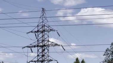 Açık mavi gökyüzüne kurulmuş yüksek voltajlı iletim kulesinin görüntüsü. Ağaçlar sahneyi çerçeveler. Ağaçları ve bulutları olan açık mavi gökyüzüne karşı yüksek voltajlı güç hatları