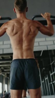 Kas yığını bir adam spor salonunda barfiks egzersizi yapıyor, dayanıklılık ve zindelik gösterisi yapıyor. Spor salonunda spor yapan sağlıklı bir adamın dikey bir çubuğa yanaşması.