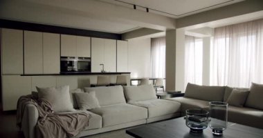 Tarafsız tonlarla donatılmış şık ve şık bir modern minimalist oturma odası, rahat bir bölüm koltuğu, ve arka planda iyi düzenlenmiş bir mutfak alanı, dingin bir lüks duygusu ifade ediyor..