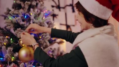 Noel ağacını altın takılarla süsleyen şenlikli bir kadın. Evde tatil sezonunun neşesini ve sıcaklığını yakalıyor. Noel Ağacı 'nı Altın Mücevherlerle süsleyen Kadın