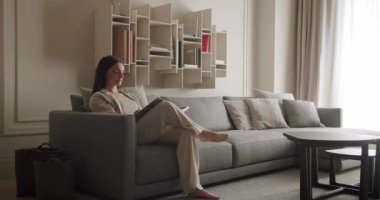Bir kadın, modern, minimalist bir koltuğa rahatça oturur ve kitap okur. Oturma odasında sakin ve rahat bir atmosferi teşvik eden tarafsız tonlar ve şık bir dekor var. Kadın Okuma Kitabı