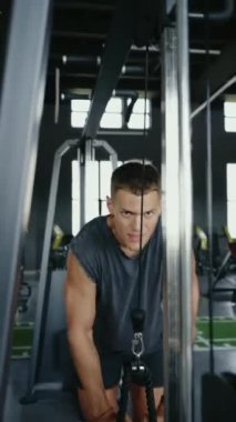 Genç adam, modern bir spor salonunda kablo makinesiyle antrenmanına odaklanıyor. Fitness ve dayanıklılık eğitimi konsepti. Üst Vücut Güçlendirme Dikey Jimnastik Salonu 'nda Kablo Makinesi ile Odaklanmış Adam Egzersizi