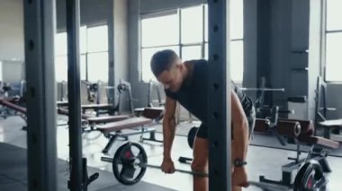 Adam modern, iyi donanımlı ve doğal ışık alan bir spor salonunda ağırlık kaldırıyor. Fitness, güç antrenmanı ve egzersiz konsepti. Modern Güç Eğitiminde Kararlı Adam Ağırlık Kaldırıyor