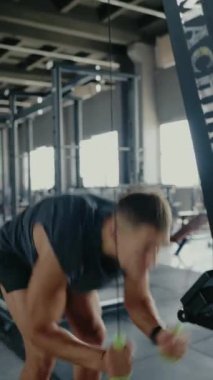 Spor salonundaki atletik adam halat makinesiyle yoğun egzersiz yapıyor. Profesyonel ekipmanlarla modern bir fitness tesisinde fitness ve dayanıklılık eğitimine odaklanın. Dikey Çalışan Odaklanmış Adam
