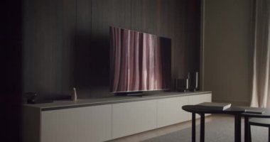 Duvara monte edilmiş düz ekran televizyon, minimalist mobilyalar ve ince dekorlu modern oturma odası. Oda sakin ve sofistike bir ortam yayıyor. Düz Ekran TV ile Modern Oturma Odası