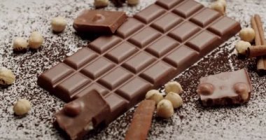 Beyaz bir yüzeyde fındık ve tarçın çubuklarıyla çevrili sütlü çikolatanın yakın çekimi. Tarifler, pazarlama ve yemek blogları için mükemmel. Şekerlemenin zarafetini yakala.