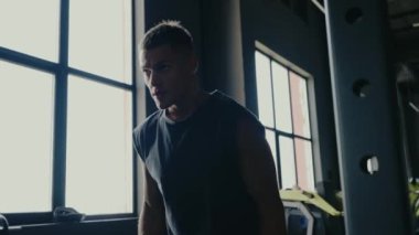 Spor salonunda halter kaldırmaya odaklanmış genç bir adam güç ve kararlılık sergiliyor. Modern Spor Salonu 'nda Halterle Çalışan Odaklanmış Adam. Erkek Silueti Çalışıyor