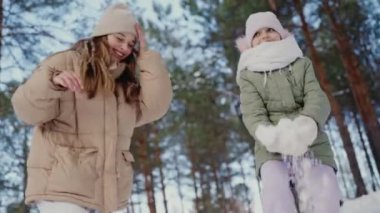 İki kız kış ormanında karda neşeyle oynuyorlar, ağaçlarla kaplı bir gölgeliğin altında bir an gülüşlerini ve mutluluklarını yakalıyorlar. Neşeli Kış Anları: Yağan Karda Oynayan İki Kız