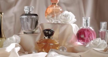 Çeşitli zarif parfüm şişeleri ve ipek kumaş üzerinde beyaz güllerin yer aldığı lüks bir sergi. Yumuşak ışıklandırma, zarif ve sofistike atmosferi geliştirir. Güzellik ve lüks için mükemmeldir. 