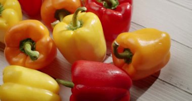 Beyaz ahşap bir yüzey üzerinde canlı kırmızı, sarı ve turuncu dolma biberler sergilenmektedir. Biber renkleri parlak ışıkta canlı bir şekilde parlıyor, tazeliklerini ve dokularını sergiliyorlar..