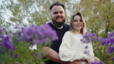 Güzel genç bir çift, canlı mor çiçeklerle çevrili verimli bir bahçede sevgi dolu bir kucaklaşmayı paylaşıyor. Bu görüntü gerçek bir sevgi ve neşe anı yakalar, aşk teması için mükemmeldir.