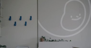 İçinde büyük bir karikatür duvar sanatı ve canlı mavi duvar kancaları olan minimalist dekorasyonlar olan modern bir ofis. Tarafsız tonlar ve temiz çizgiler küçük bir bitki tarafından tamamlanır.