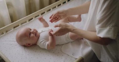 Anne kadın, bebek beşikteki güzel bebeğine nazik bir masaj yapıyor. Annelik hayatı. Bebek bakımı konsepti. Anne, bebeğine yatakta masaj yapıyor. Anne oynuyor ve bebeğe masaj yapıyor.