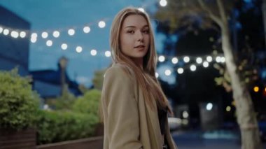 Genç bir kadın, alacakaranlıkta sessiz bir şehir parkında arkasında parlayan tel ışıklarıyla yakalanır. Sakince kameraya bakıyor, sakin ve düşünceli bir ruh hali içinde..