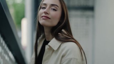Kendine güvenen genç bir kadın, güneşli bir günde sakin ve kendine güvenen rahat bir ceketle dışarıda poz veriyor. Güneşli bir günde, rahat ceketli, kendine güvenen genç bir kadın.