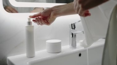 Modern ve temiz bir banyo ortamında sabunluk kullanan yakın plan bir el fotoğrafı. Görüntü hijyenik ve minimalist bir estetiği yansıtıyor. Temiz tuvaletteki sabun dağıtıcısını kullanan ellerin yakın çekimi.
