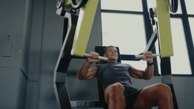 Modern bir jimnastik salonunda spor yapan bir adam, spor salonuna ve güç toplamaya odaklanıyor. Modern Spor Salonunda Güçlü Eğitim Makinesi Üzerinde Egzersiz Yapan Adam