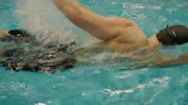 Yüzme havuzunun berrak, turkuaz sularına dalmış, rekabetçi yüzmenin yoğunluğunu ve hareketini yakalayan bir yüzücünün güçlü bir görüntüsü. Turkuaz suyla dolu bir havuza daldırılmış.