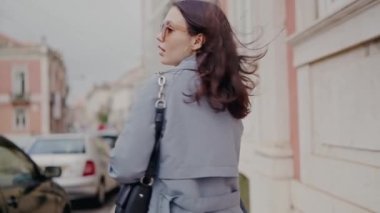Şehir caddesinde şık mavi ceketli zarif genç bir kadın akıllı telefon kullanıyor. Şehir yaşamında moda ve teknoloji. Şehirde Akıllı Telefonlu Moda Genç Kadın Yürüyüşü