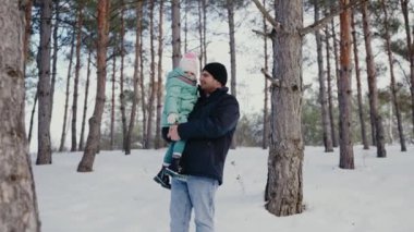 Karlı bir çam ormanında kızını kaldıran bir babanın yürek ısıtan görüntüsü. Bu an, kış boyunca ailenin neşesini ve bağını yakalar. Karlı Orman 'da Baba Tutucu Bebek, Aile Kışı