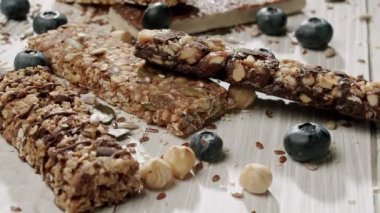 Tahta arka planda çeşitli fındıklı, tohumlu ve yaban mersinli sağlıklı granola barları besleyici atıştırmalık seçenekleri vurguluyor. Fındıklı, tohumlu ve yaban mersinli Sağlıklı Granola çikolatalarının yakın çekimi