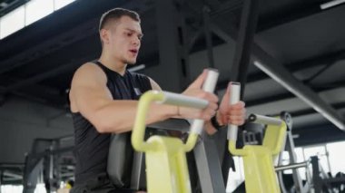 Spor giyim sektöründe odaklanmış genç bir adam modern bir spor salonunda direnç eğitim ekipmanları üzerinde çalışıyor, sağlıklı yaşam tarzını ve fitness hedeflerine olan bağlılığını vurguluyor. Genç adam spor salonunda çalışıyor.